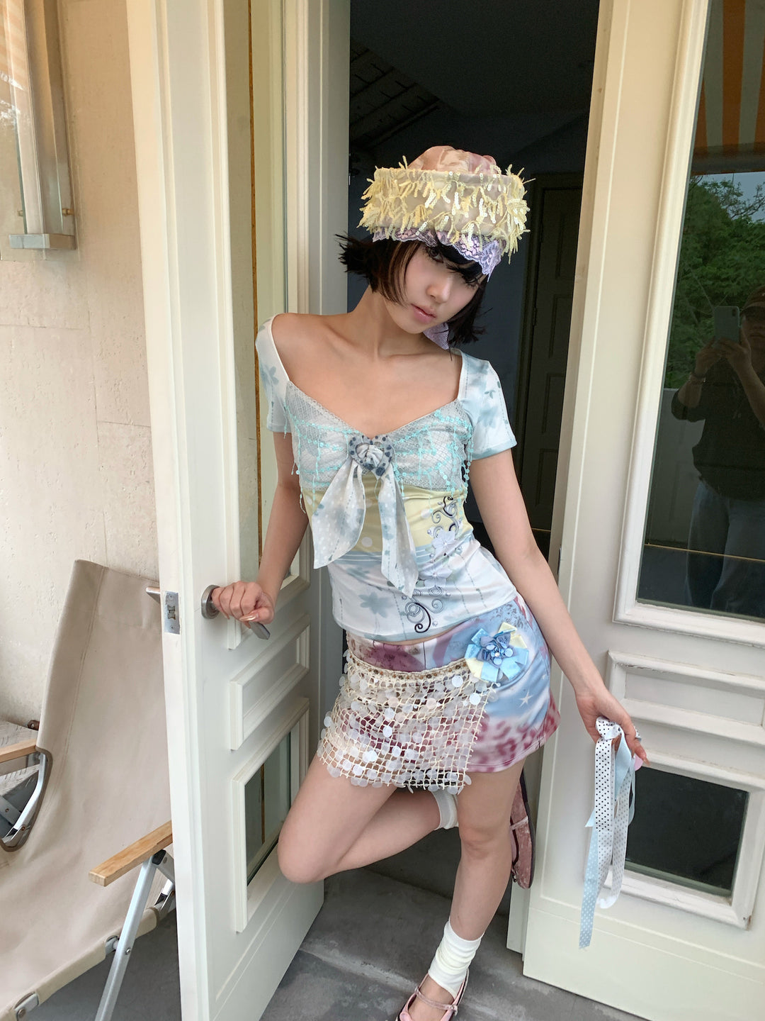 4RE1GN BLUE BLOOM patchwork short-sleeve tee in blue multicolor — front modeled view beside a doorway with a fringed hat