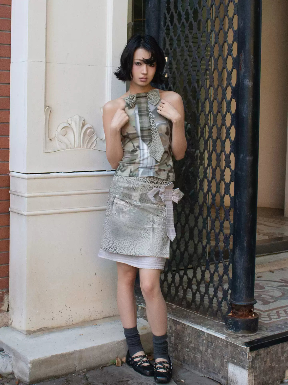 4RE1GN CROSS LEOPARD bow-detail layered skirt in beige multicolor — front modeled view beside a black metal gate