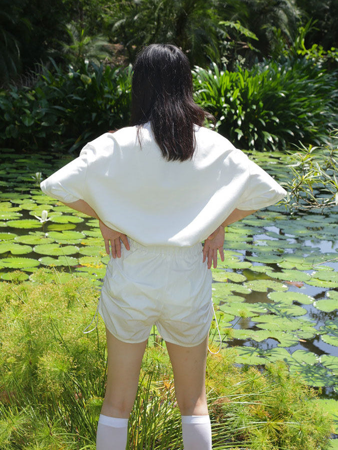 NEXT PASSPORT side-ruched drawstring mini shorts in white, outdoor back view