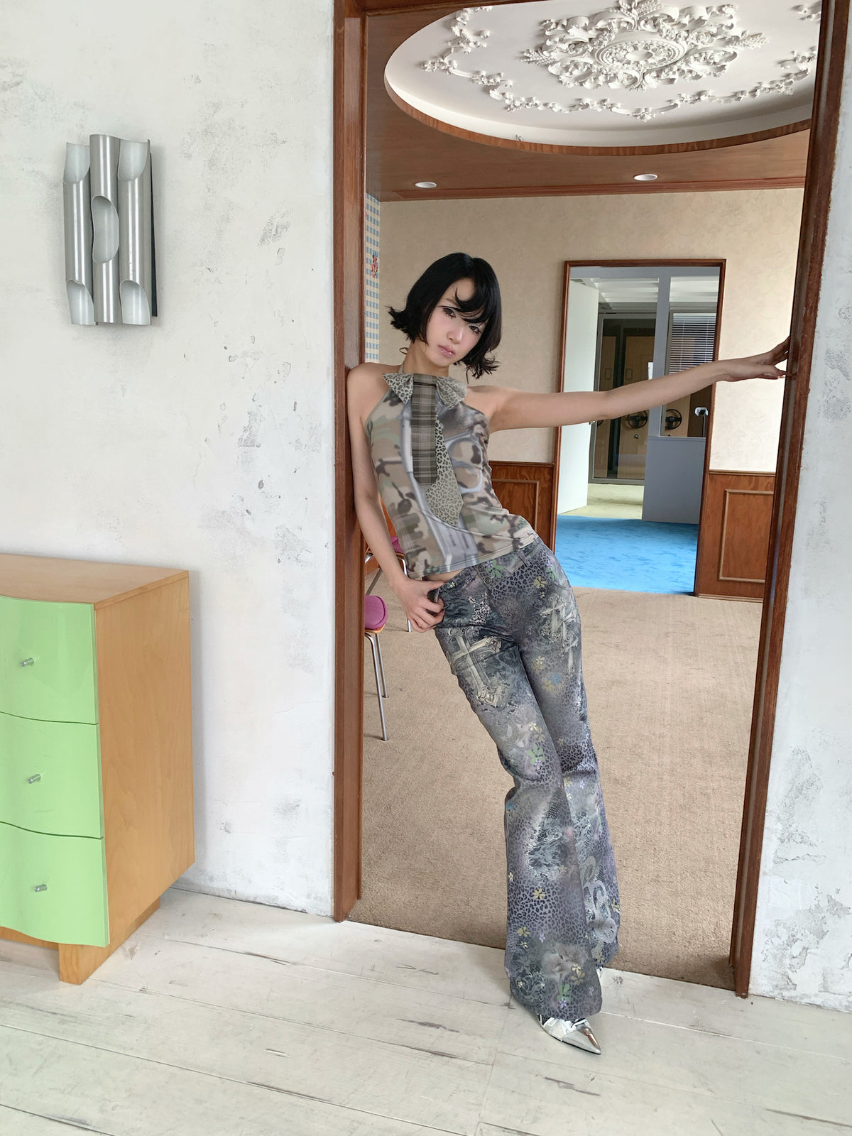 4RE1GN DEAR NINA camouflage tie-neck halter top in camo green — full-length modeled view in a doorway with one arm extended