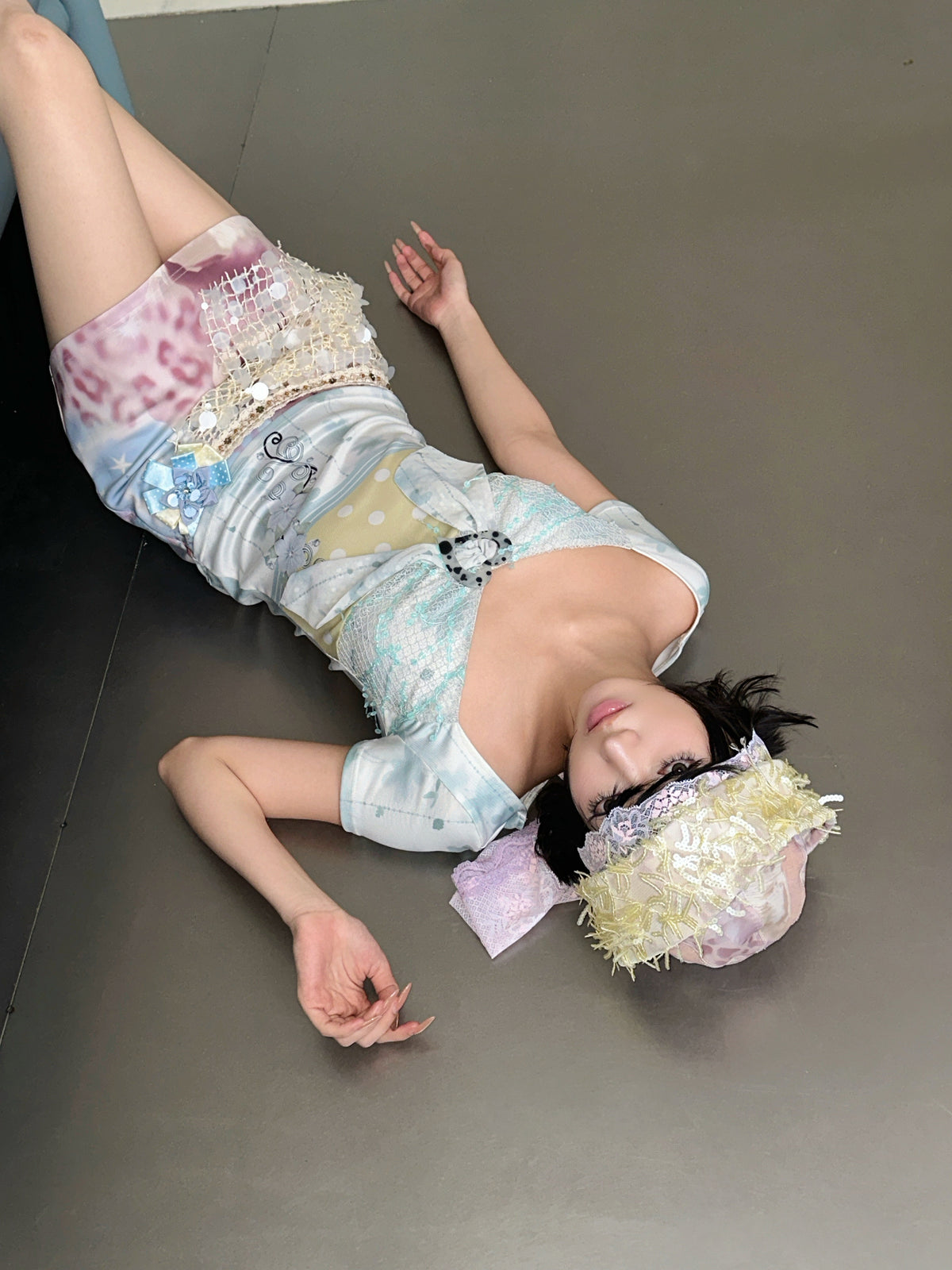 4RE1GN BLUE BLOOM patchwork short-sleeve tee in blue multicolor — modeled view reclining on the floor with a pastel mini skirt