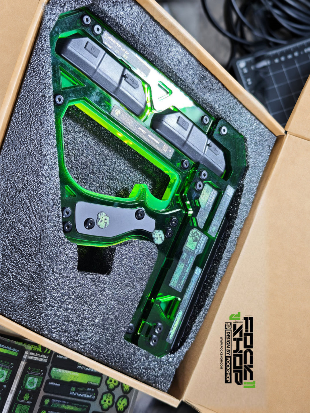 FOCKSHOP REBORN illuminated blaster prop — dark-green prop resting in fitted packaging with graphic stickers