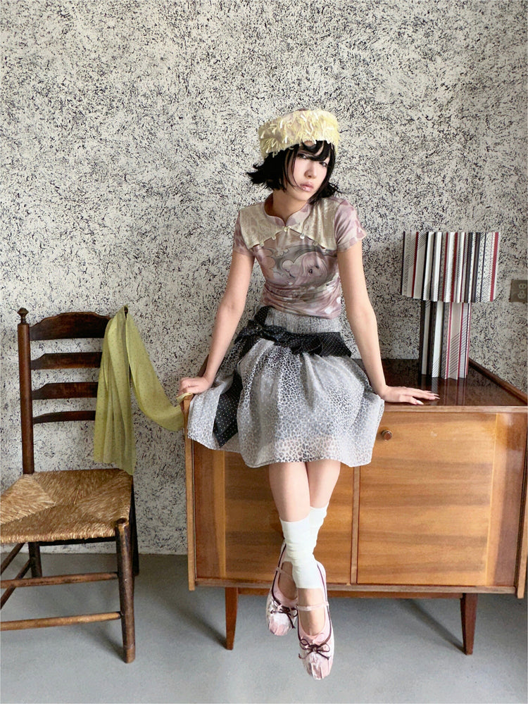4RE1GN PINK REAPER lace-panel mandarin tee in pink multicolor — seated modeled view on a wooden cabinet