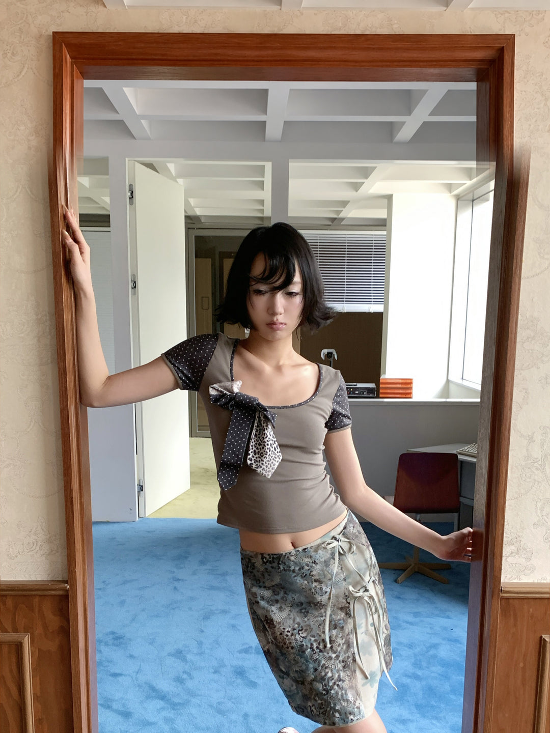 4RE1GN BLUE BLOOM tie-front layered skirt in blue multicolor — modeled view by glass doors with one arm raised