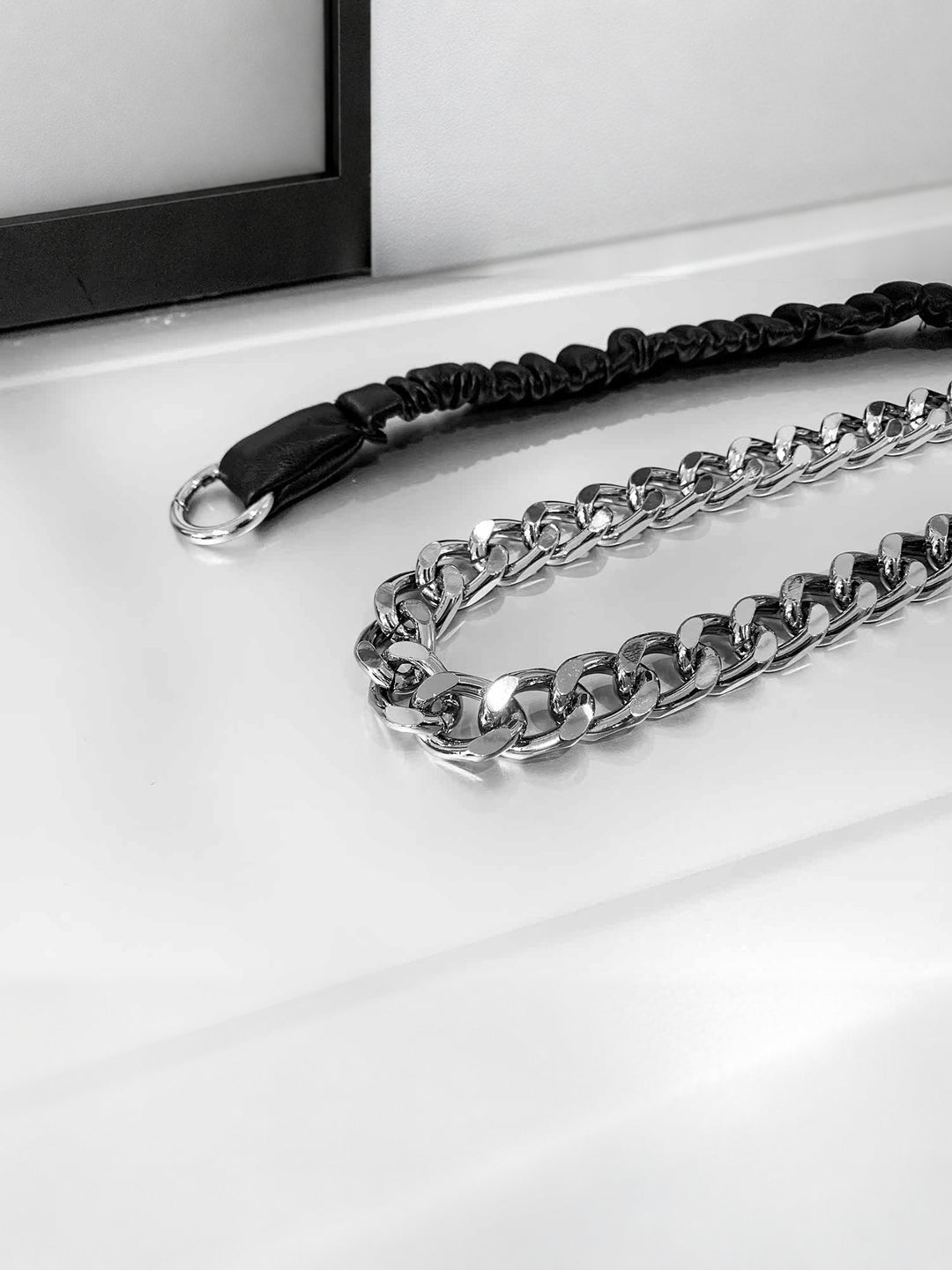 Close-up of WRAVEN belt polished silver-tone curb links beside the black gathered faux-leather strap.