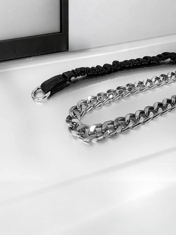 Close-up of WRAVEN belt polished silver-tone curb links beside the black gathered faux-leather strap.