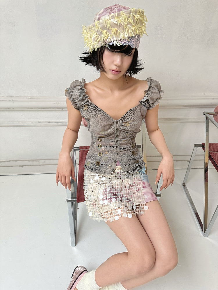 4RE1GN DREAM GARDEN sequin-panel mini skirt in pink multicolor — seated modeled view with legs crossed and a gray leopard-print top
