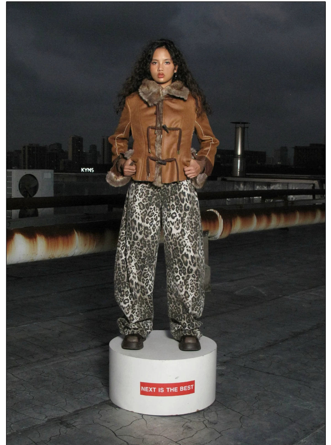 NEXT PASSPORT dark-brown rope-toggle shearling cropped jacket, nighttime rooftop full-length platform pose