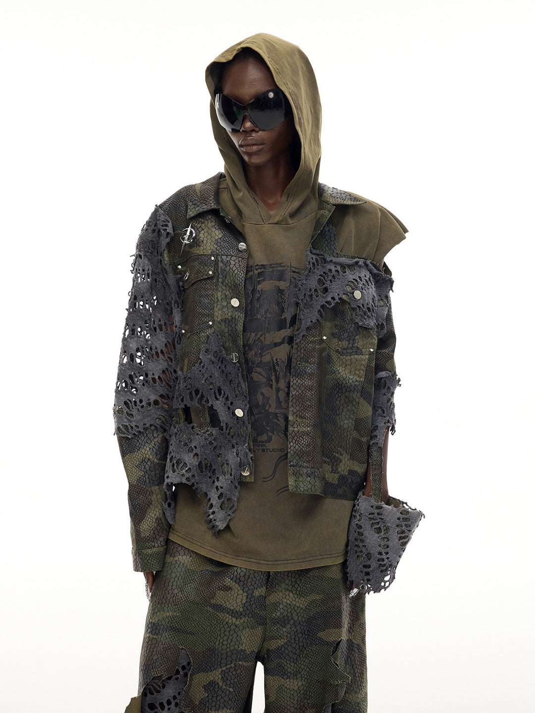 PINKSPINK ELECTRIC MOON distressed camouflage denim jacket — side-front modeled view layered over an olive hooded top