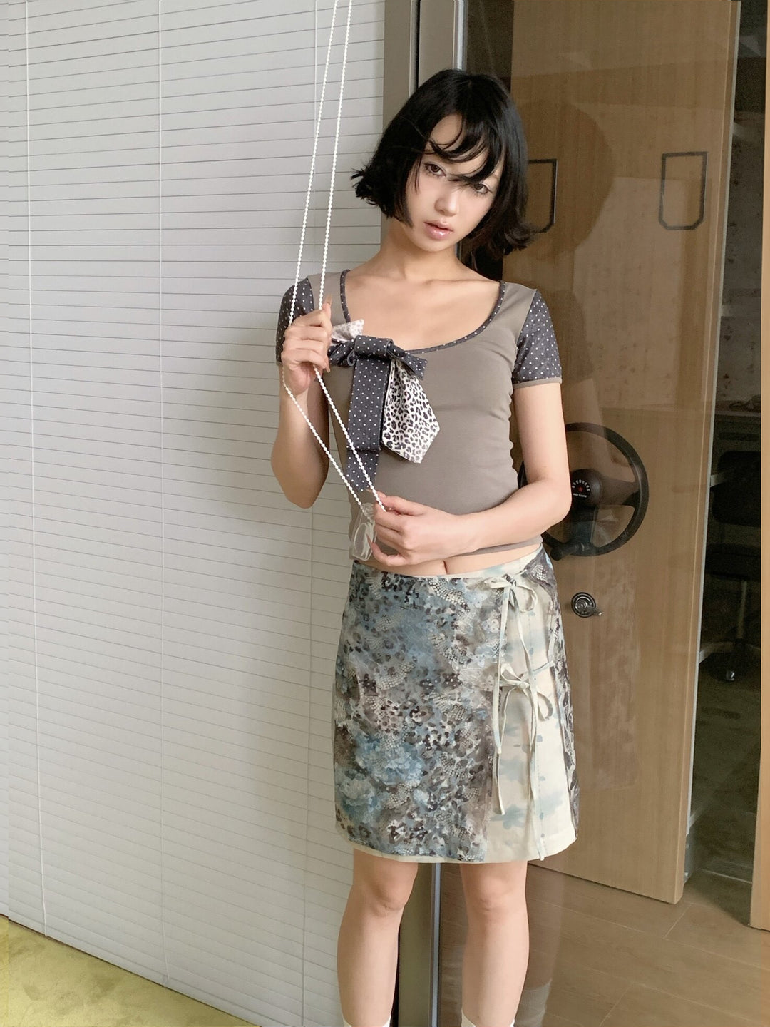 4RE1GN BLUE BLOOM tie-front layered skirt in blue multicolor — modeled view leaning beside glass doors