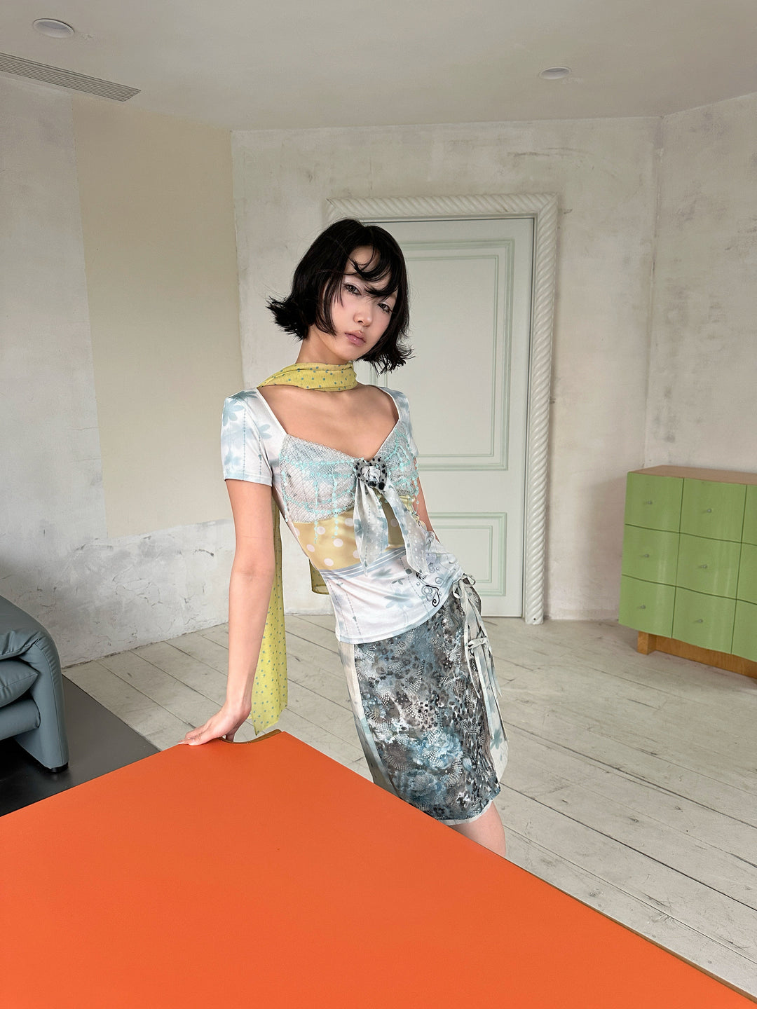 4RE1GN BLUE BLOOM tie-front layered skirt in blue multicolor — three-quarter modeled view leaning on an orange table