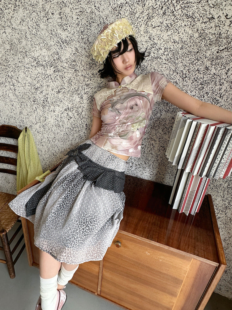 4RE1GN PINK REAPER lace-panel mandarin tee in pink multicolor — seated modeled view with an arm extended beside a lamp