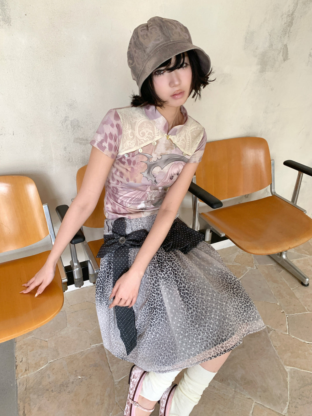 4RE1GN PINK REAPER lace-panel mandarin tee in pink multicolor — three-quarter seated modeled view with a printed bucket hat
