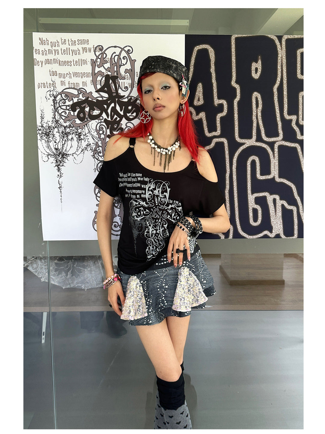 4RE1GN CROSS SCRIPT cold-shoulder tee in black — angled modeled view beside the brand display