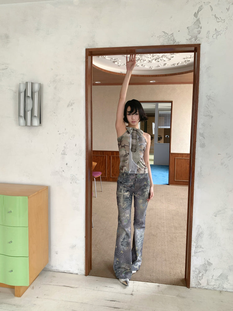 4RE1GN DEAR NINA camouflage tie-neck halter top in camo green — full-length modeled view in a doorway with one arm raised
