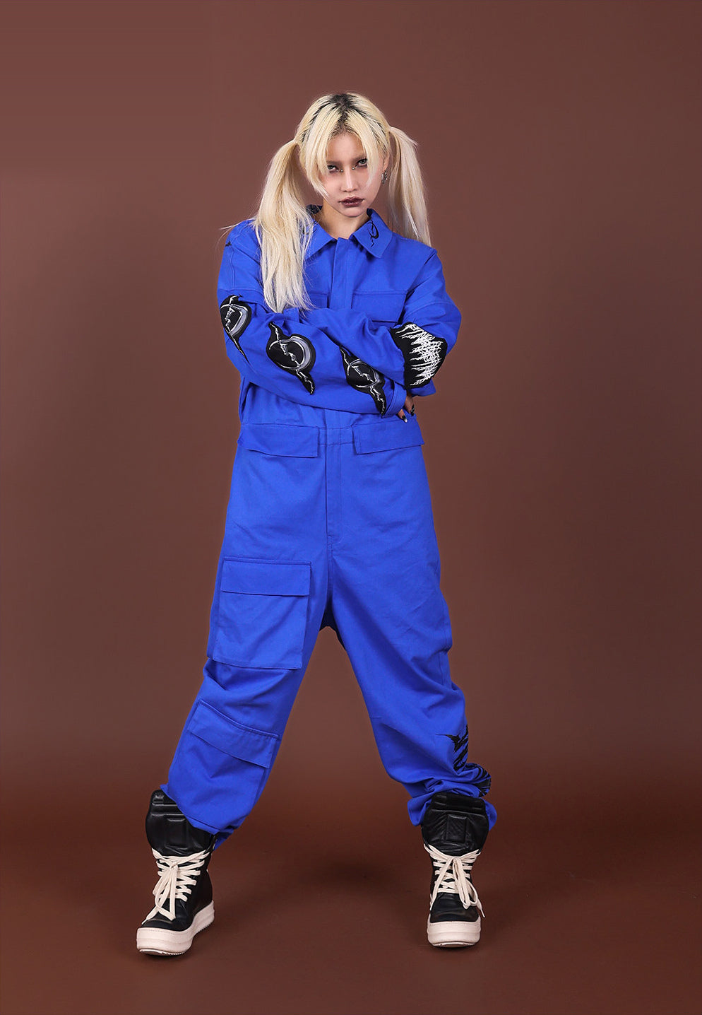 Front view of the blue REMAKE jumpsuit with arms crossed to show its Electric Moon sleeve patches