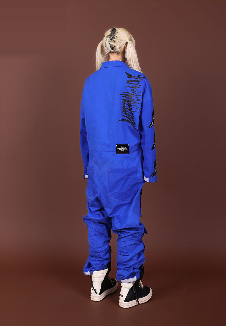 Back view of the blue REMAKE utility jumpsuit with black shoulder graphic, waist label and rear pockets