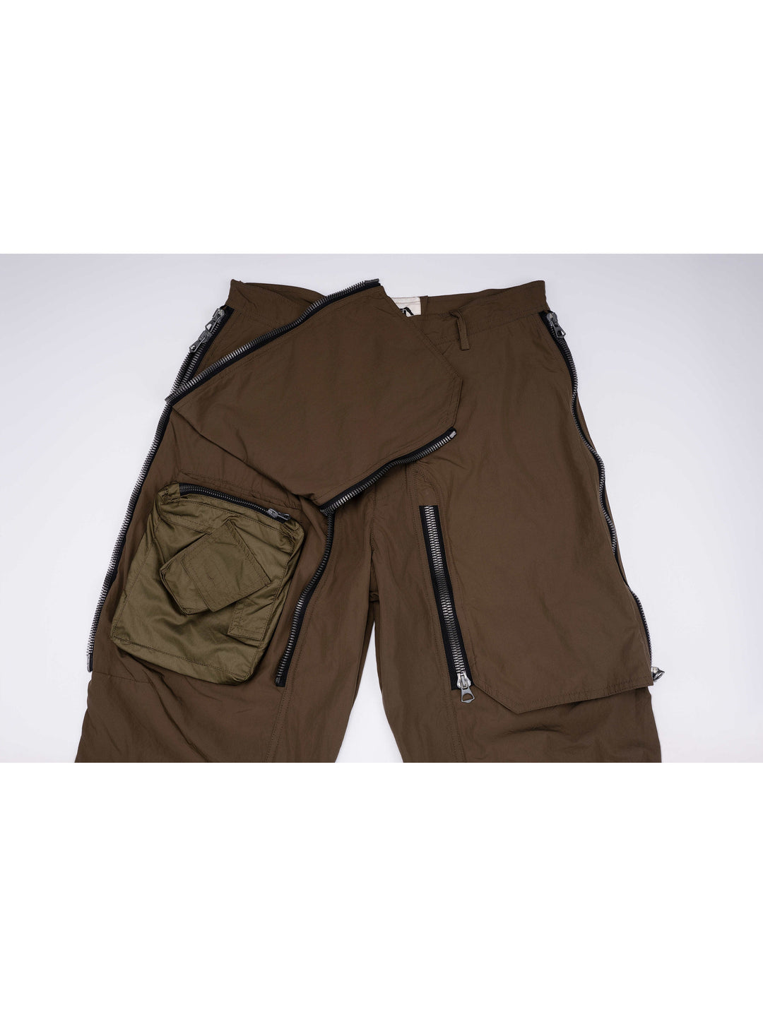 GAIA curved-blade technical pants in stone green — front upper-panel detail showing the curved zipper openings