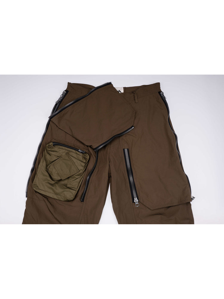 GAIA curved-blade technical pants in stone green — front upper-panel detail showing the curved zipper openings