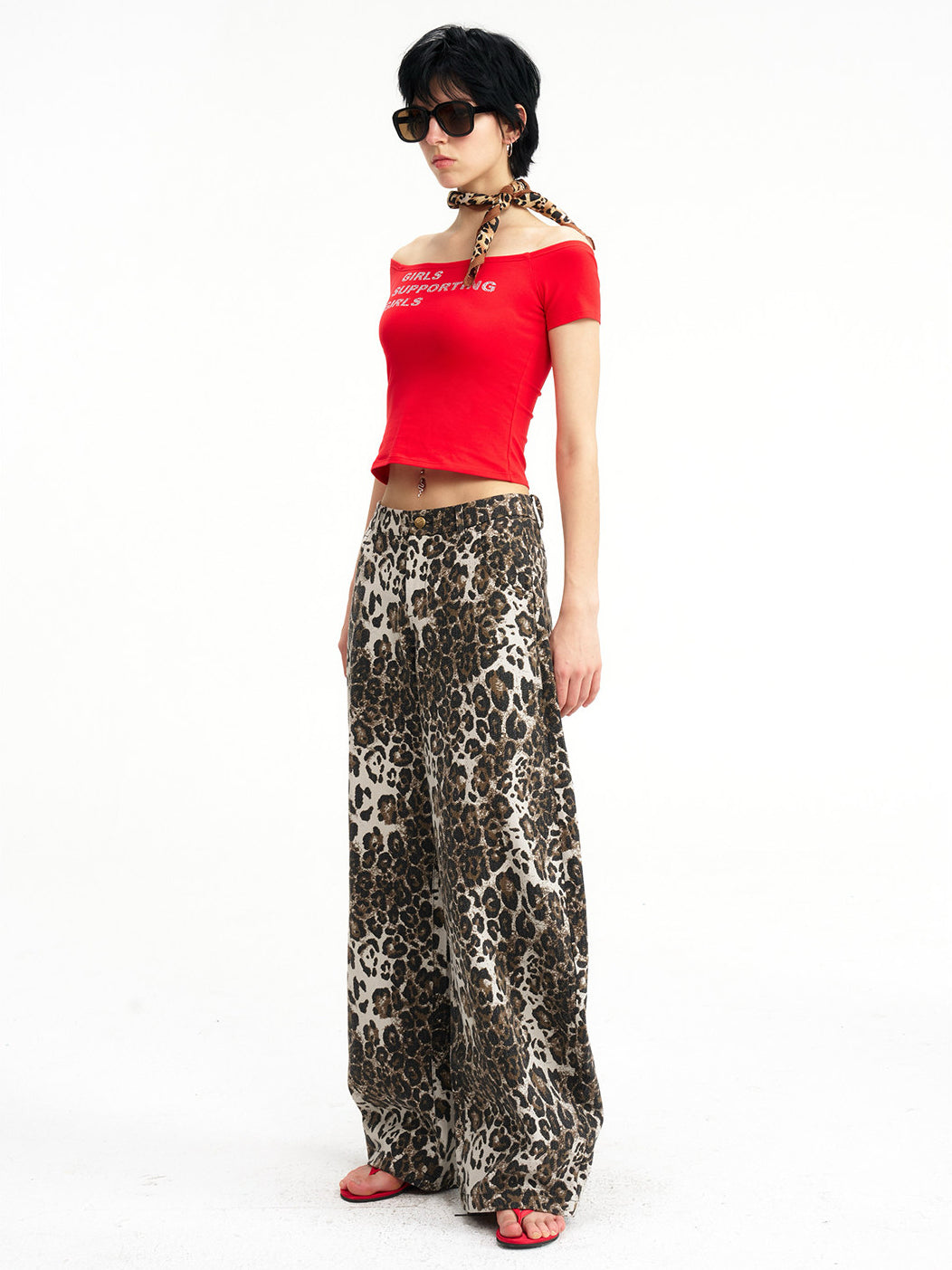 NEXT PASSPORT GIRLS SUPPORTING GIRLS rhinestone off-shoulder crop tee — red full-body modeled front view in leopard-print trousers.