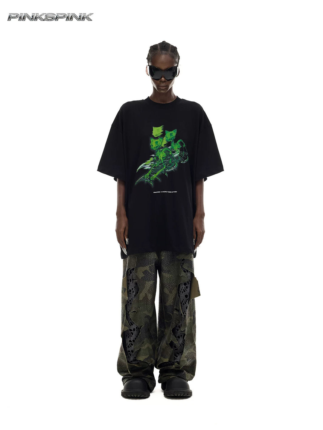 PINKSPINK MONSTER cat-skeleton oversized graphic tee in black — full-length front modeled view with the loose tee worn over separate camouflage trousers