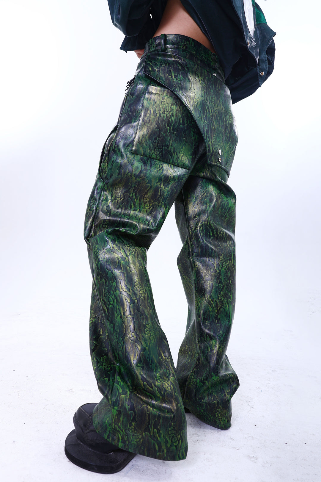 EMBRYO TRIANGLE ARMOR lace-inset leather pants in green — rear modeled view with triangular overlay, styled with a green overshirt