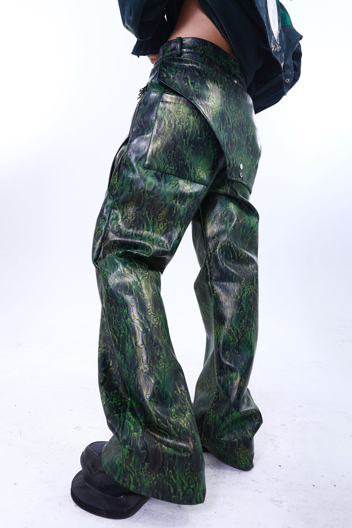 EMBRYO TRIANGLE ARMOR lace-inset leather pants in green — rear modeled view with triangular overlay, styled with a green overshirt