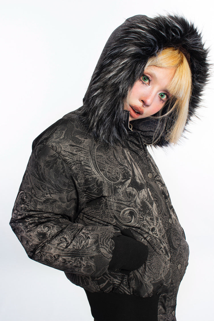 4RE1GN GOTHIC down jacket in charcoal ornamental print — Hood-up side three-quarter close-up with hand in pocket.
