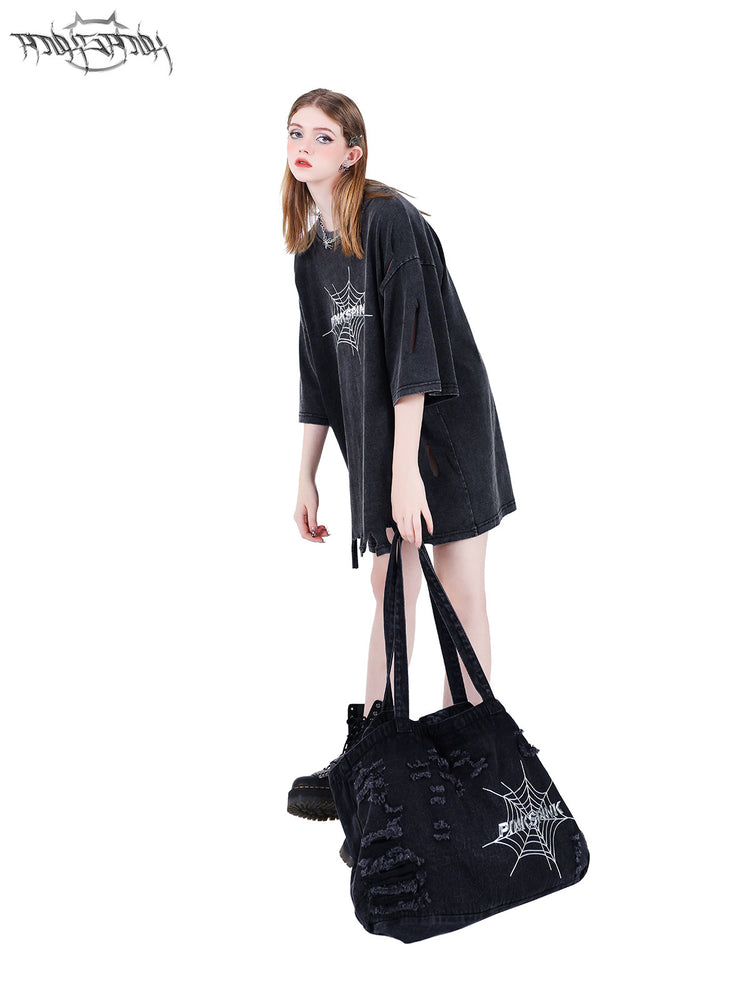 PINKSPINK SPIDER distressed denim shoulder tote — front modeled view holding the tote beside the legs