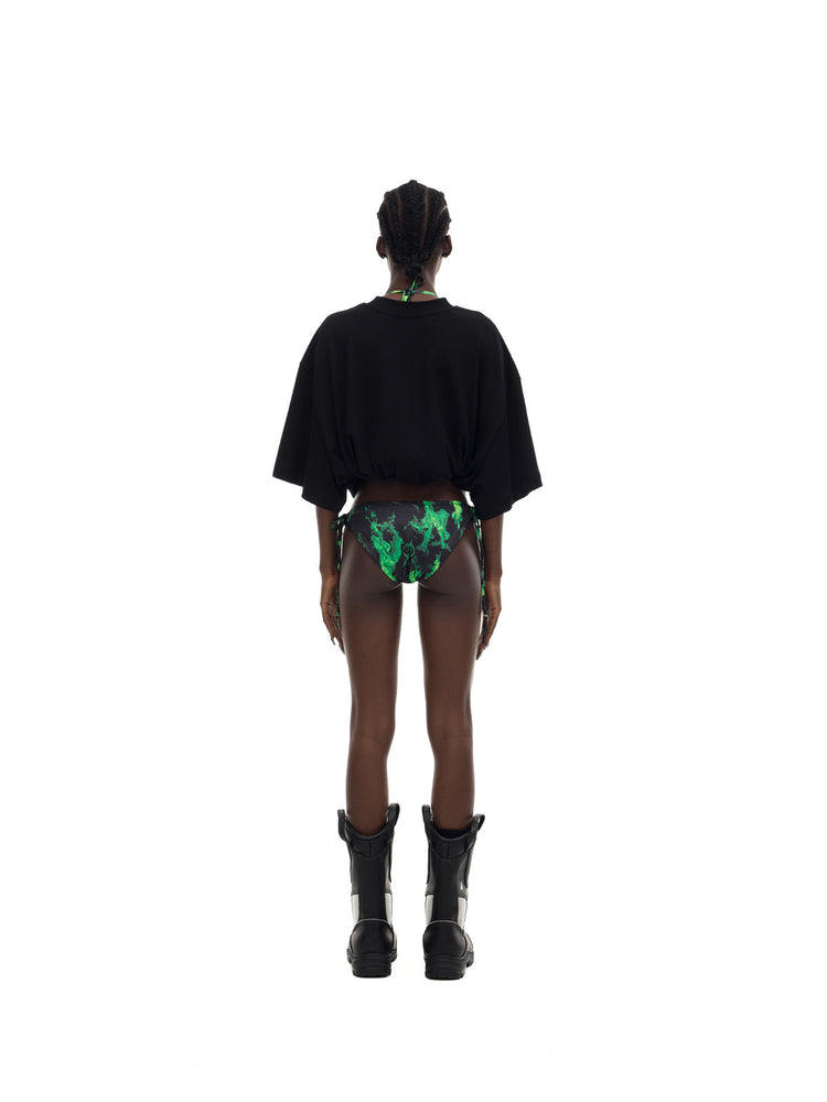 PINKSPINK MONSTER cat-skeleton oversized graphic tee in black — full-length rear modeled view with the hem rolled up over separate printed bottoms