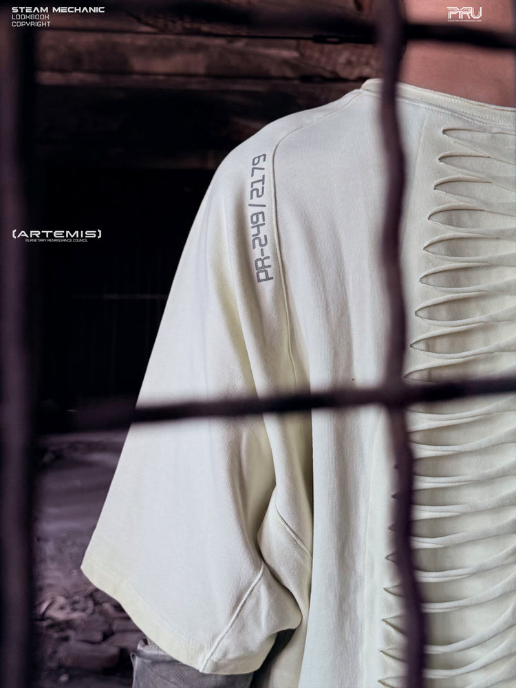 ERODED SPINE distressed asymmetric tee in aurora green — close-up of the shoulder code and spine-like cutouts through a foreground wire grid