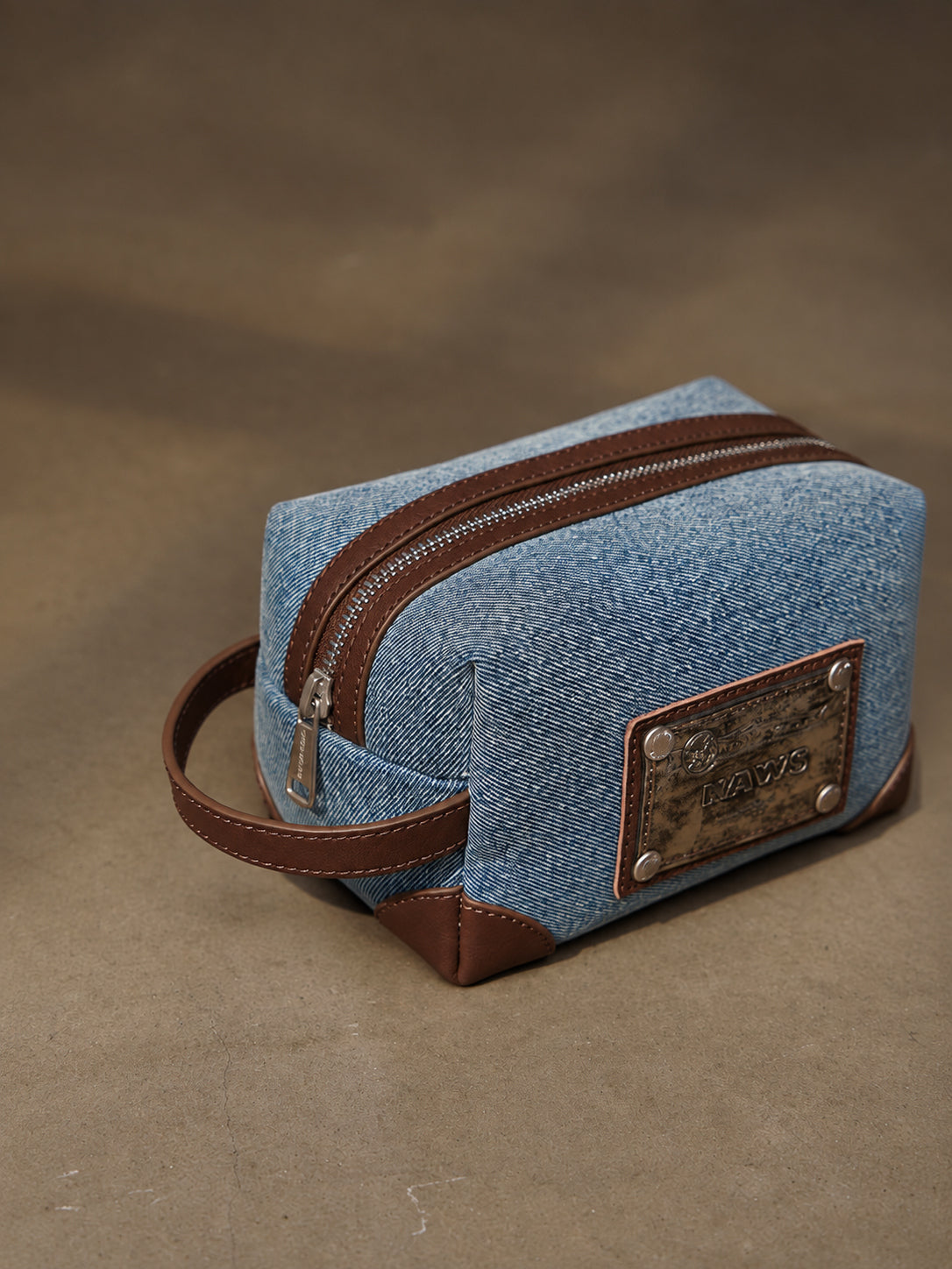 NAWS BLUE BOX denim makeup bag — three-quarter view with zipper, side handle and brown corner panels