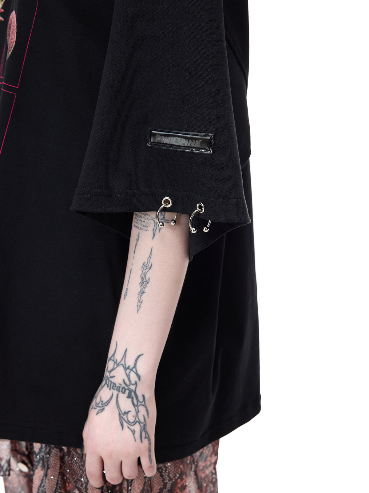 PINKSPINK PLANT PUNK oversized graphic tee in black — close detail of the sleeve logo patch, eyelets and silver-tone rings