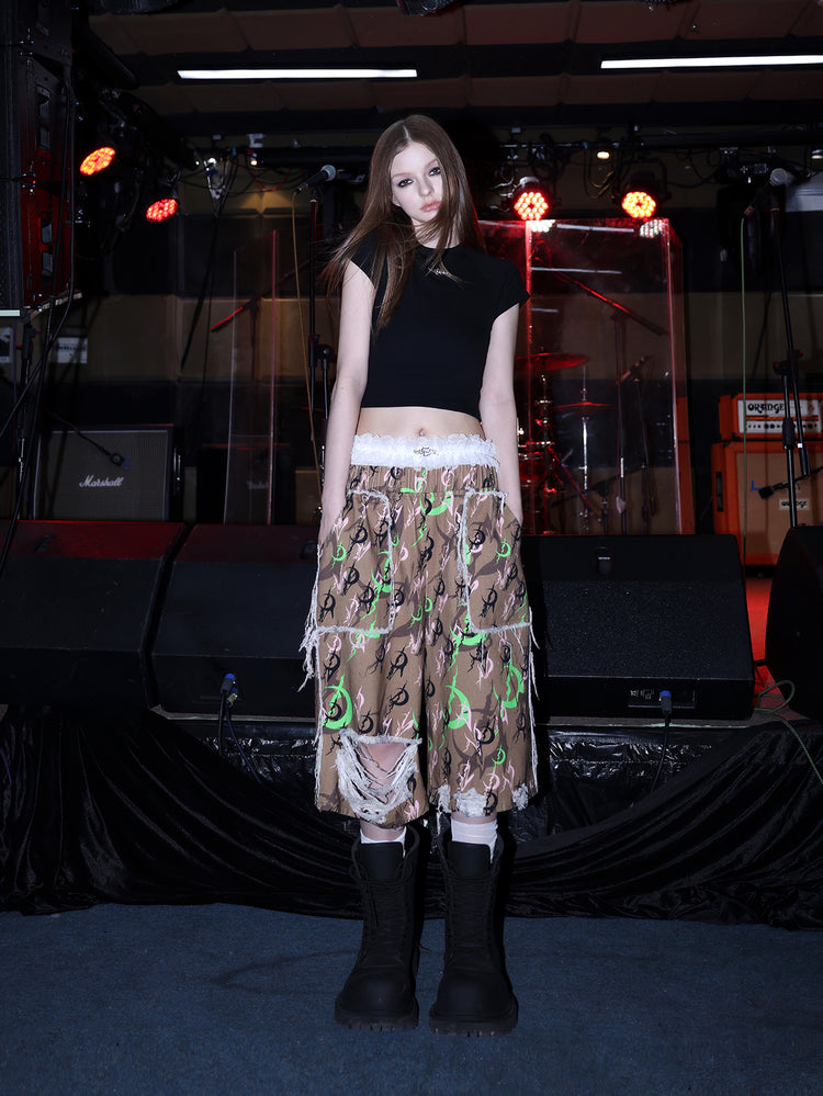 PINKSPINK ELECTRIC MOON distressed camo cropped trousers in CAMOUFLAGE — angled full front with white lace accessory.