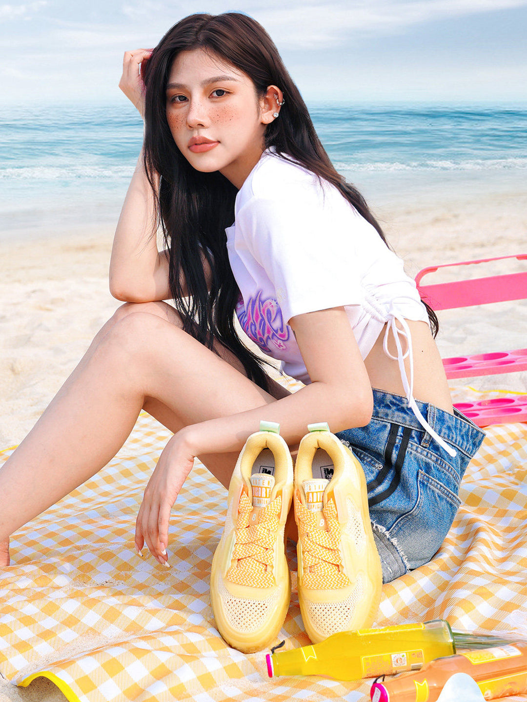 STARTER ICE DRINK Orange sneakers beside a seated model on a beach picnic blanket, showing open-knit uppers and broad yellow laces