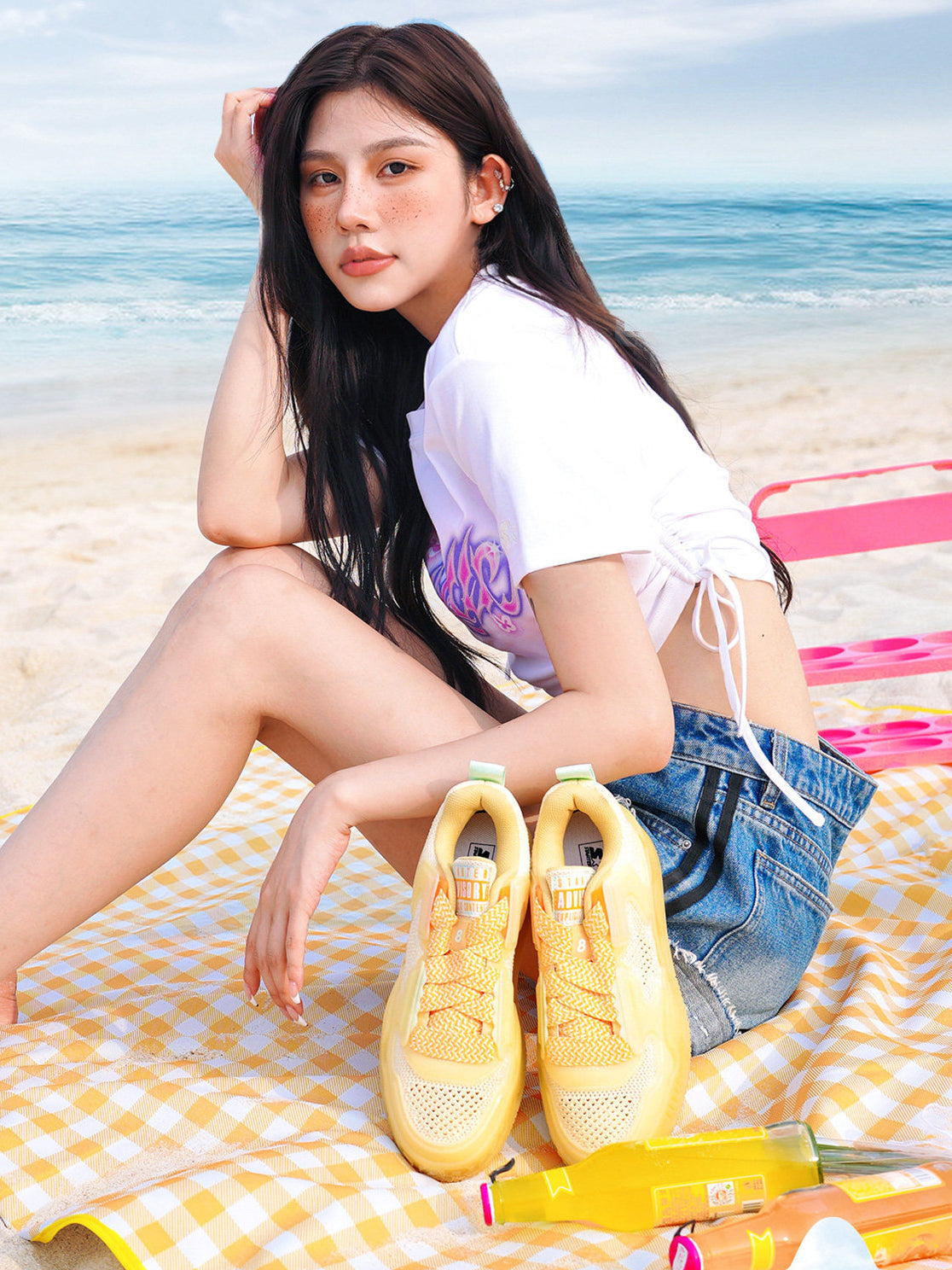 STARTER ICE DRINK Orange sneakers beside a seated model on a beach picnic blanket, showing open-knit uppers and broad yellow laces