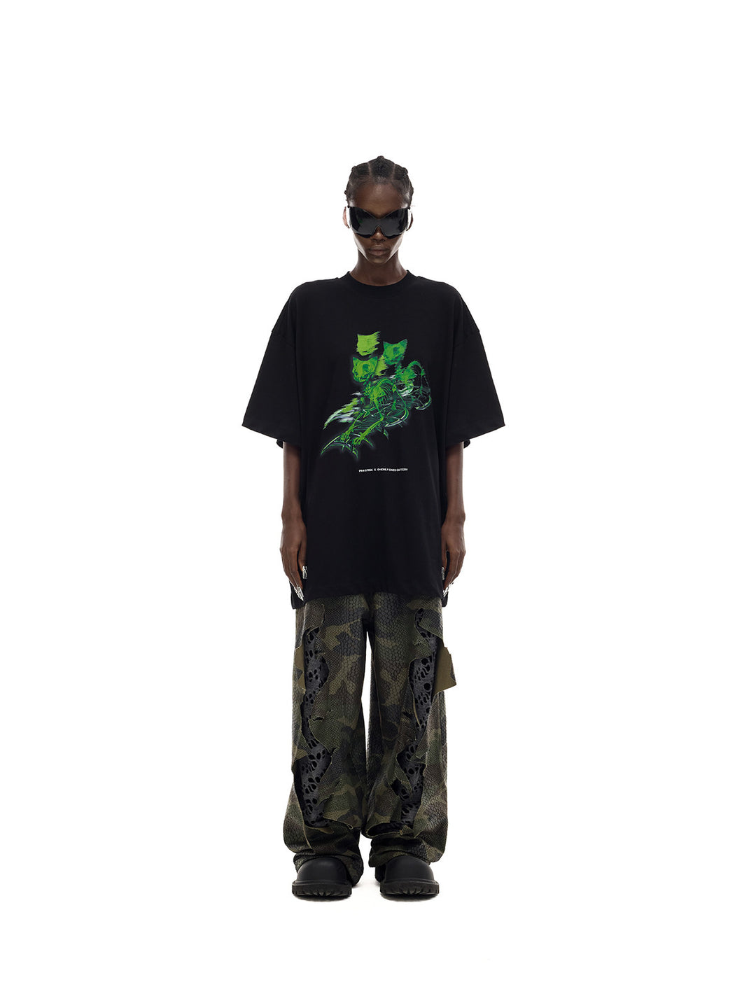PINKSPINK MONSTER cat-skeleton oversized graphic tee in black — straight-on full-length front modeled view over separate camouflage trousers