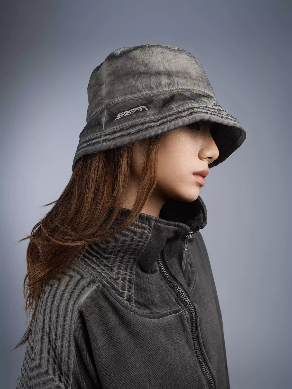 PIONEER distressed nylon bucket hat in moon dust gray — three-quarter modeled portrait showing the washed crown and logo