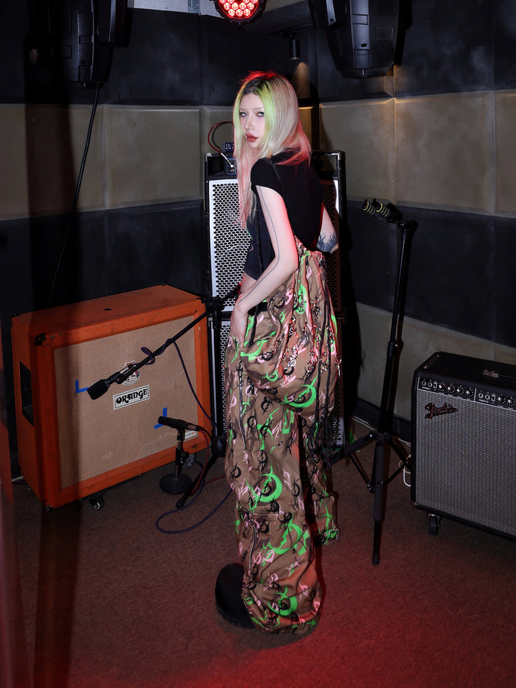 PINKSPINK ELECTRIC MOON sculpted camo cargo trousers in CAMOUFLAGE — side full-body beside an amplifier.