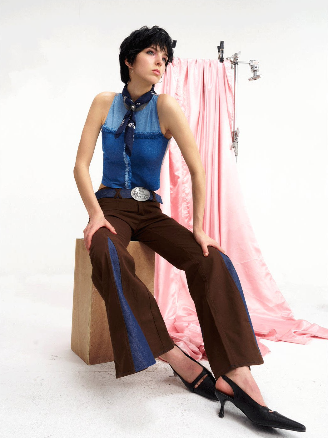 NEXT PASSPORT denim-panel low-rise flared pants in brown — seated front editorial view.