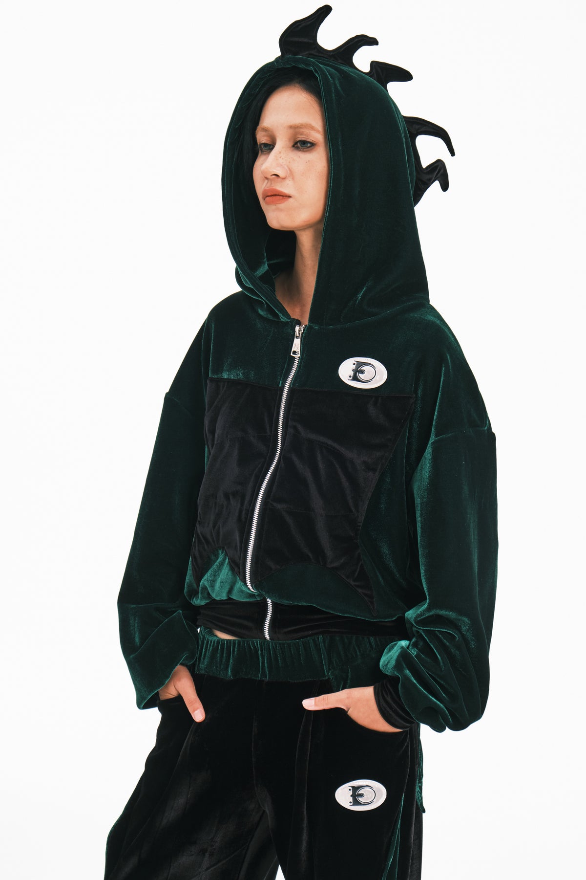 EMBRYO GREEN SPIKE cropped velvet hoodie in green — three-quarter front modeled view with the hood up and hands in pockets