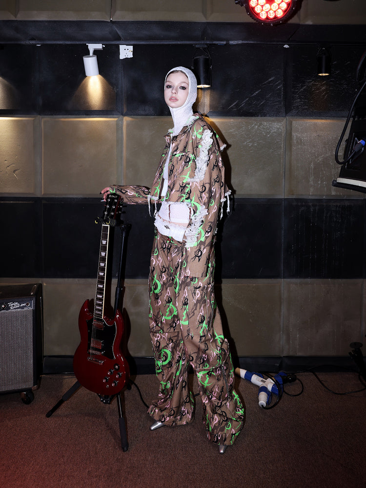 PINKSPINK ELECTRIC MOON sculpted camo cargo trousers in CAMOUFLAGE — side full-body beside a guitar.
