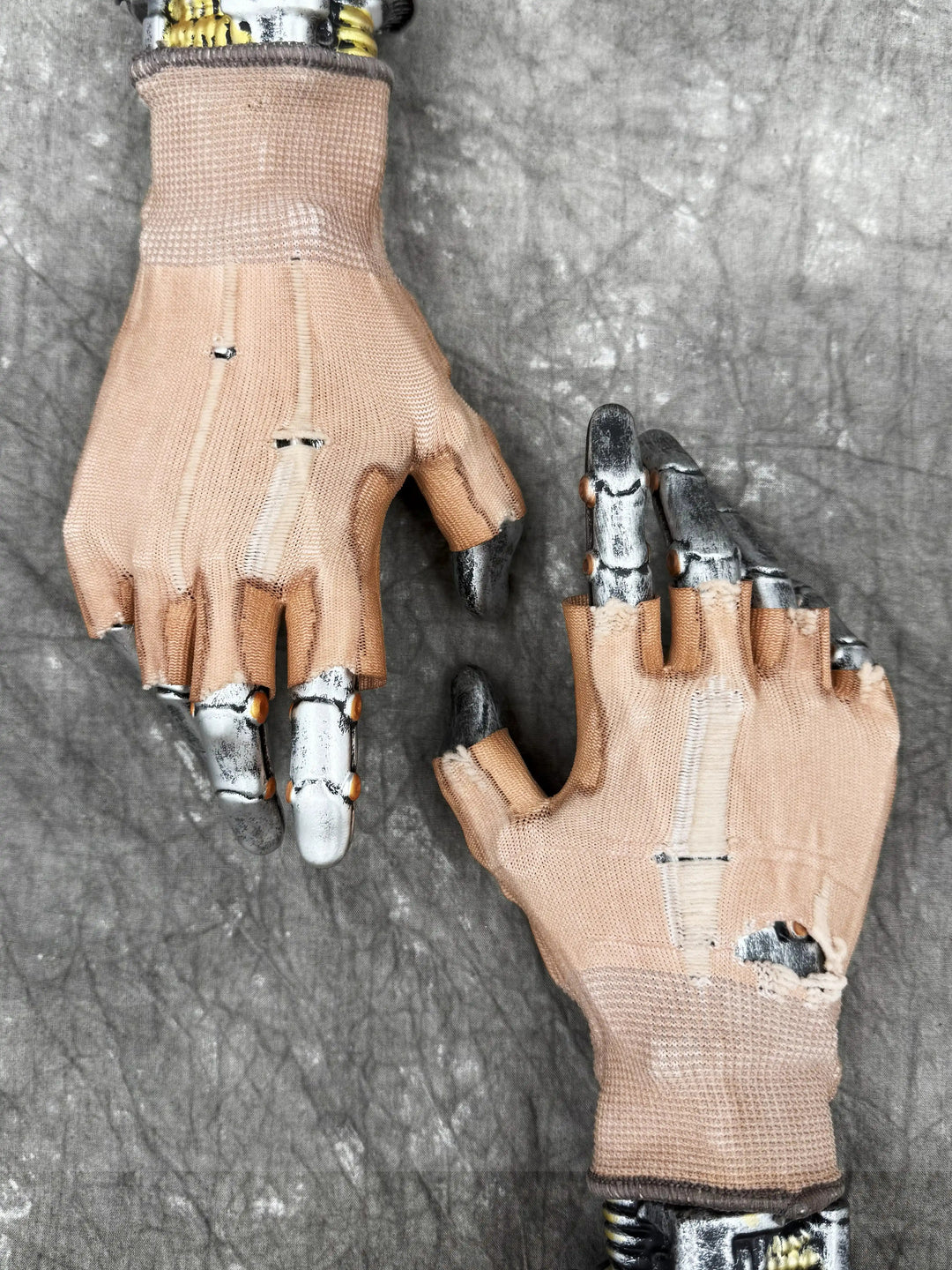 PRECISION CASTING distressed fingerless gloves in soft orange — flat-lay on metal display hands showing the distressed cotton knit and open fingertips