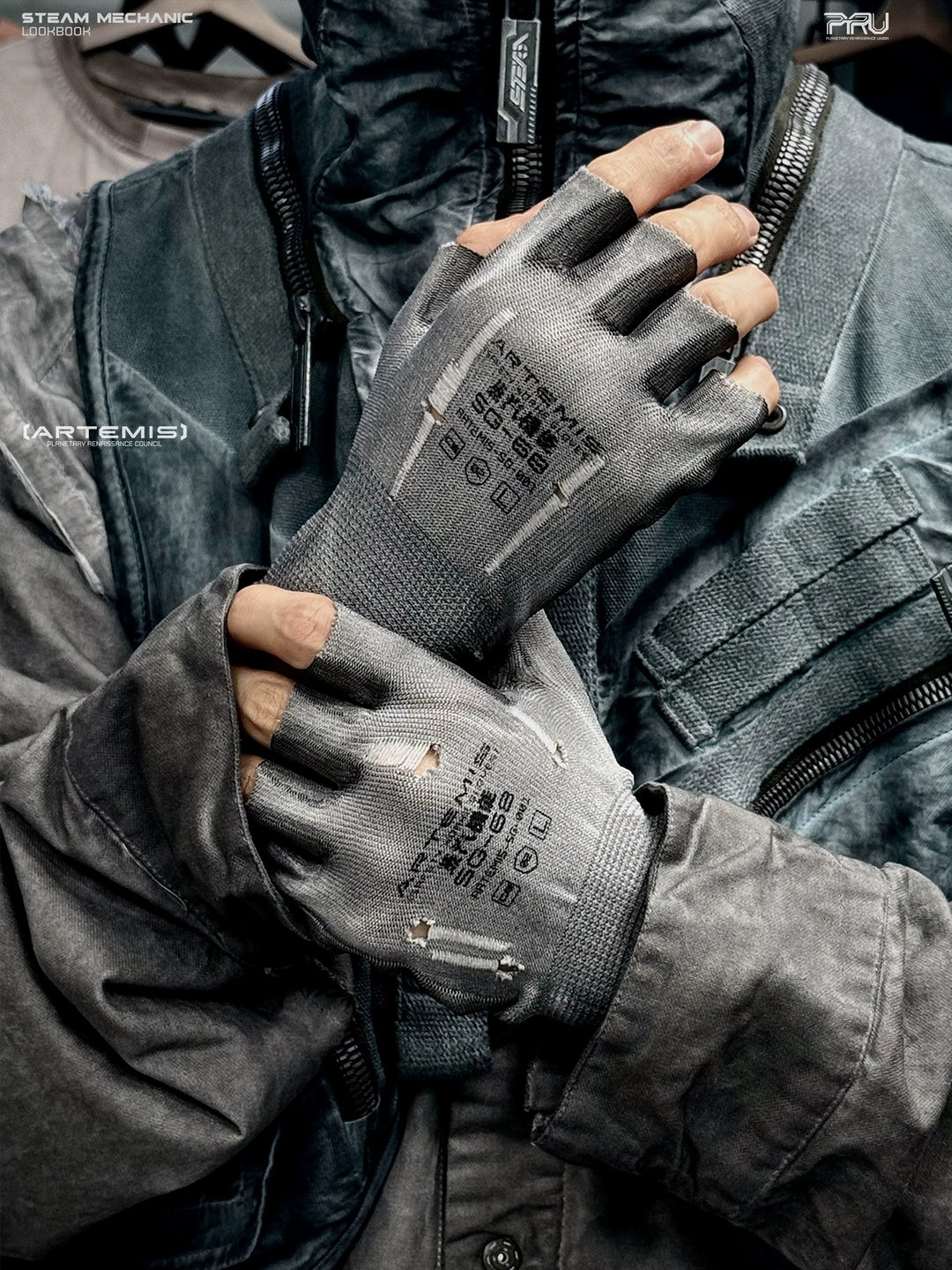 STEAM FUNCTION PRECISION CASTING distressed fingerless gloves in moon-dust gray — modeled close-up with hands crossed over the chest, showing distressed knit and printed backs