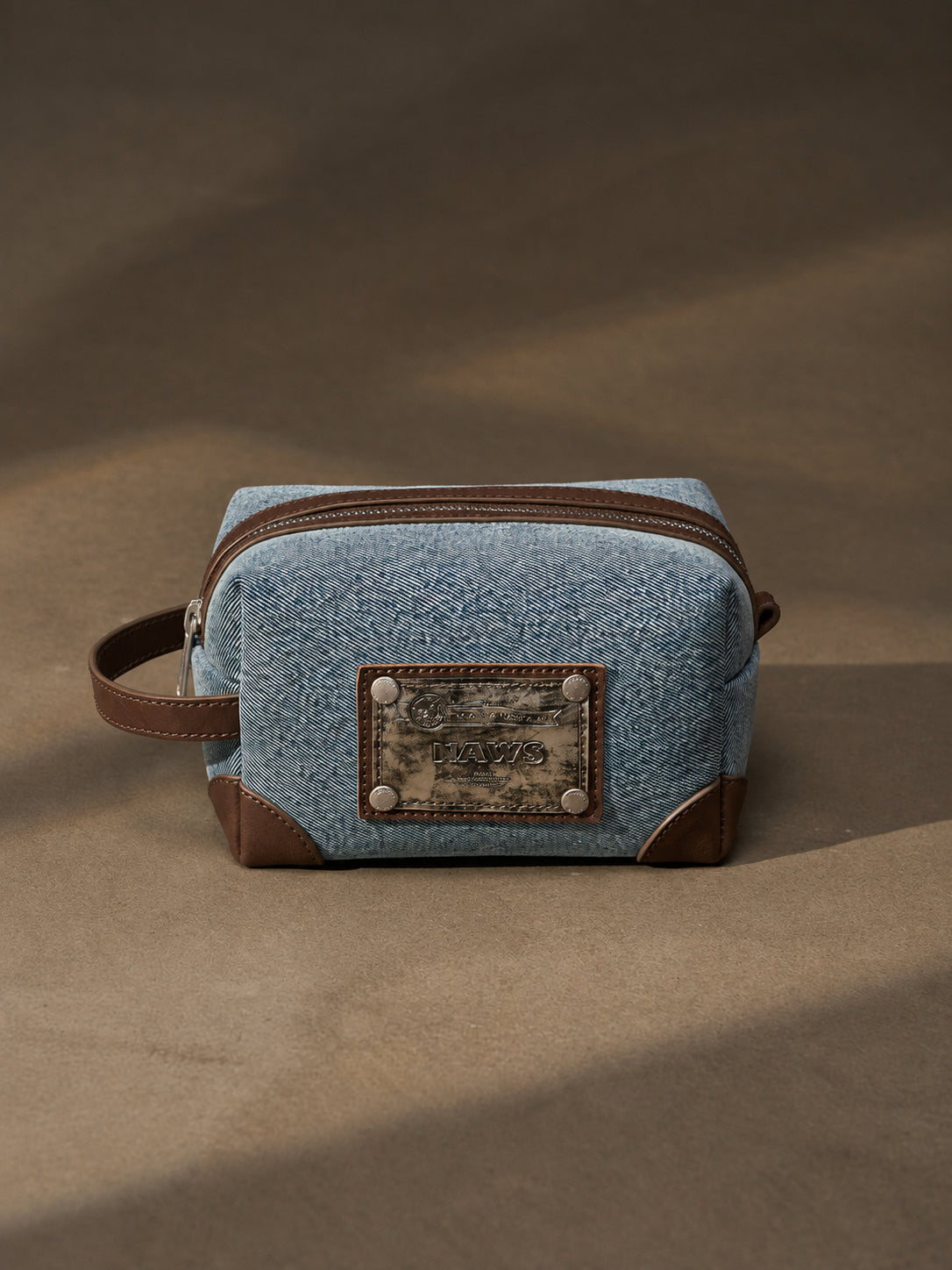 NAWS BLUE BOX denim makeup bag — front view with logo plaque and zip closure