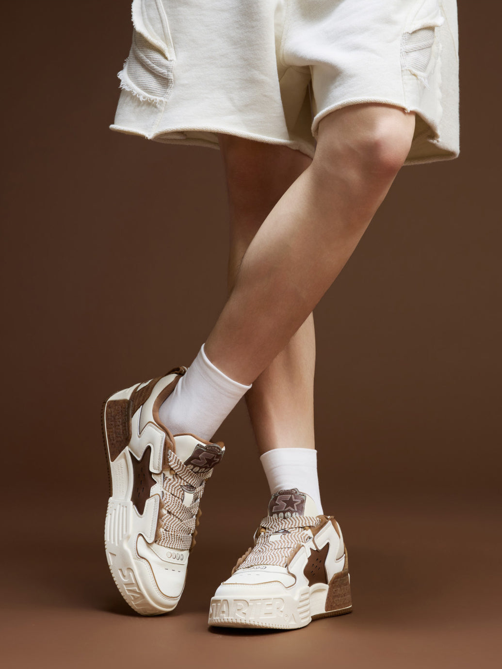 STARTER VOL 90S LATTE angled front and inner-side on-foot views highlighting coffee-toned TPU trim and toe graphics