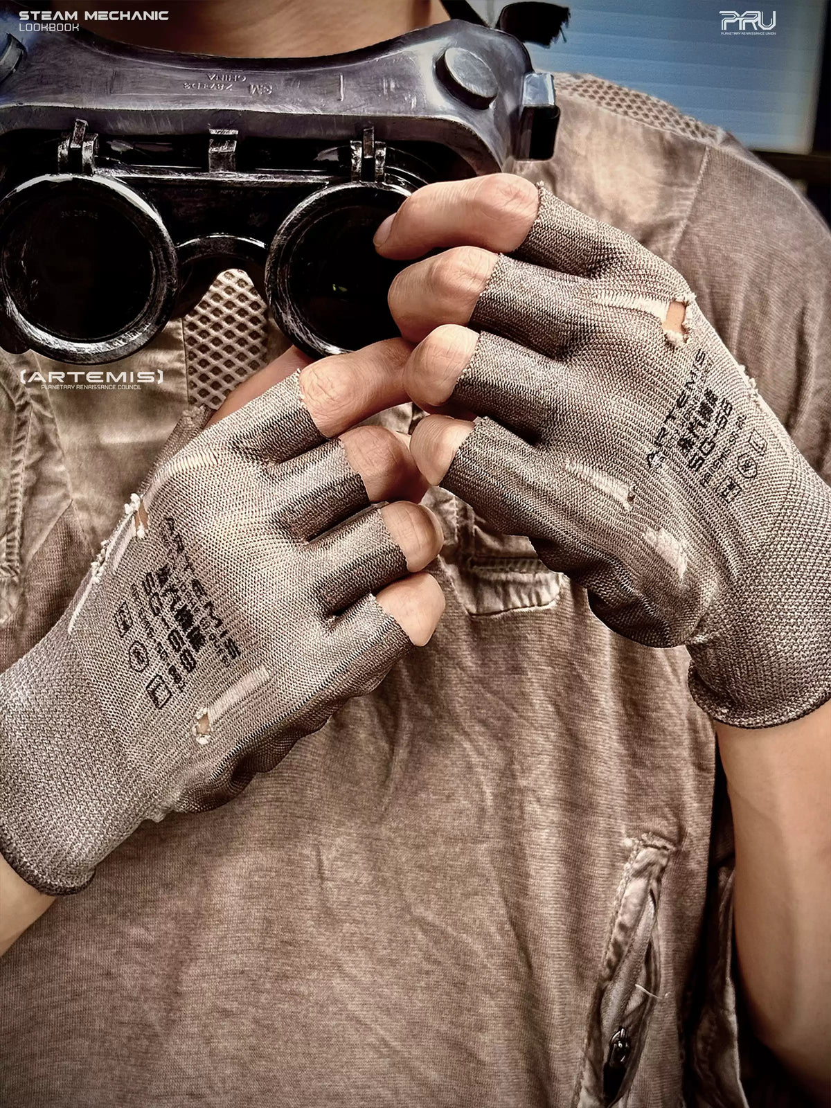 STEAM FUNCTION PRECISION CASTING distressed fingerless gloves in brown-gray — modeled close-up holding goggles, showing printed backs and frayed finger openings
