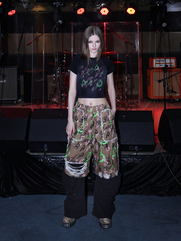 PINKSPINK ELECTRIC MOON distressed camo cropped trousers in CAMOUFLAGE — full front layered over black trousers.