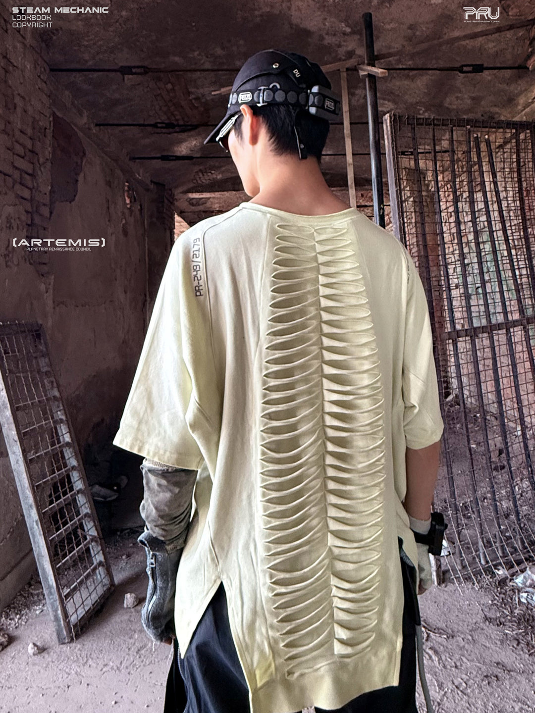 ERODED SPINE distressed asymmetric tee in aurora green — rear three-quarter view showing the extended cutout back panel