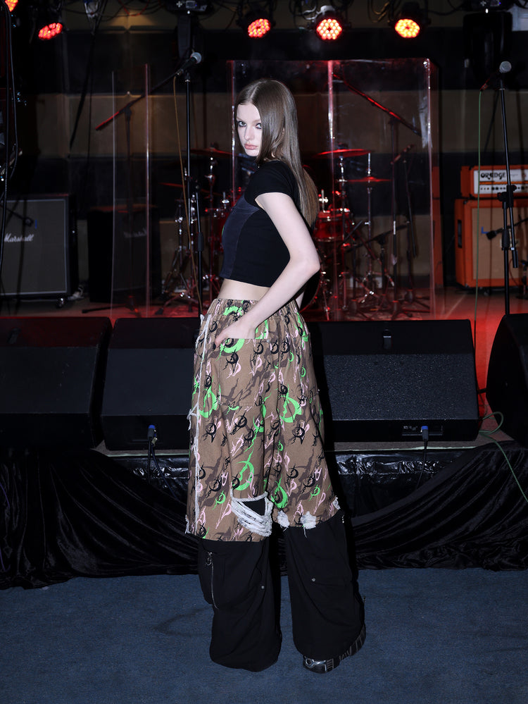 PINKSPINK ELECTRIC MOON distressed camo cropped trousers in CAMOUFLAGE — side full-body layered over black trousers.